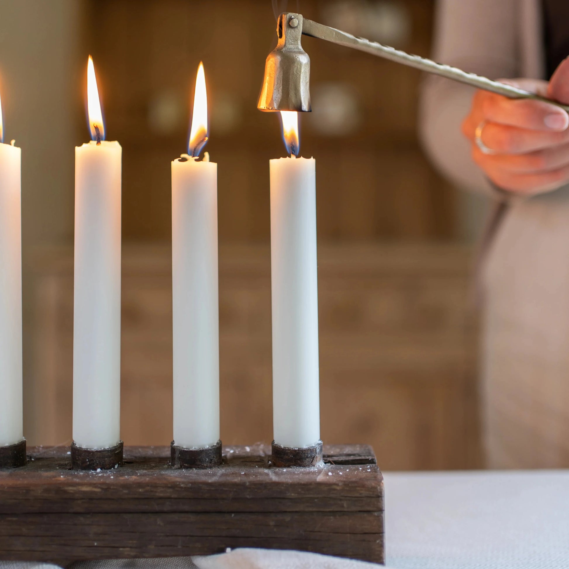 Candle holder with lit candles being tended to by a person using a candle snuffer.