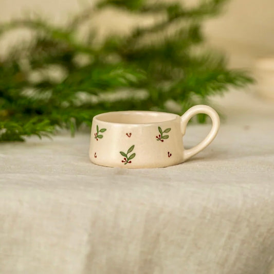 Small ceramic cup with floral patterns on a textured surface with greenery in the background