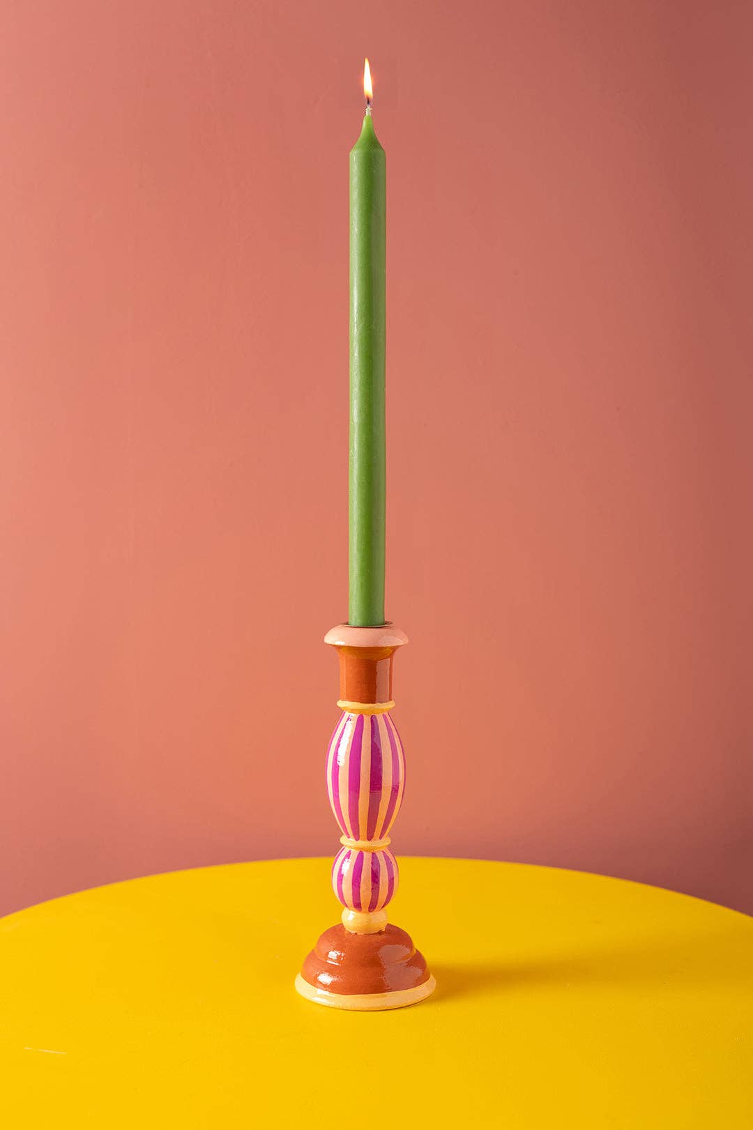 Decorative candlestick with a green candle on a pink background