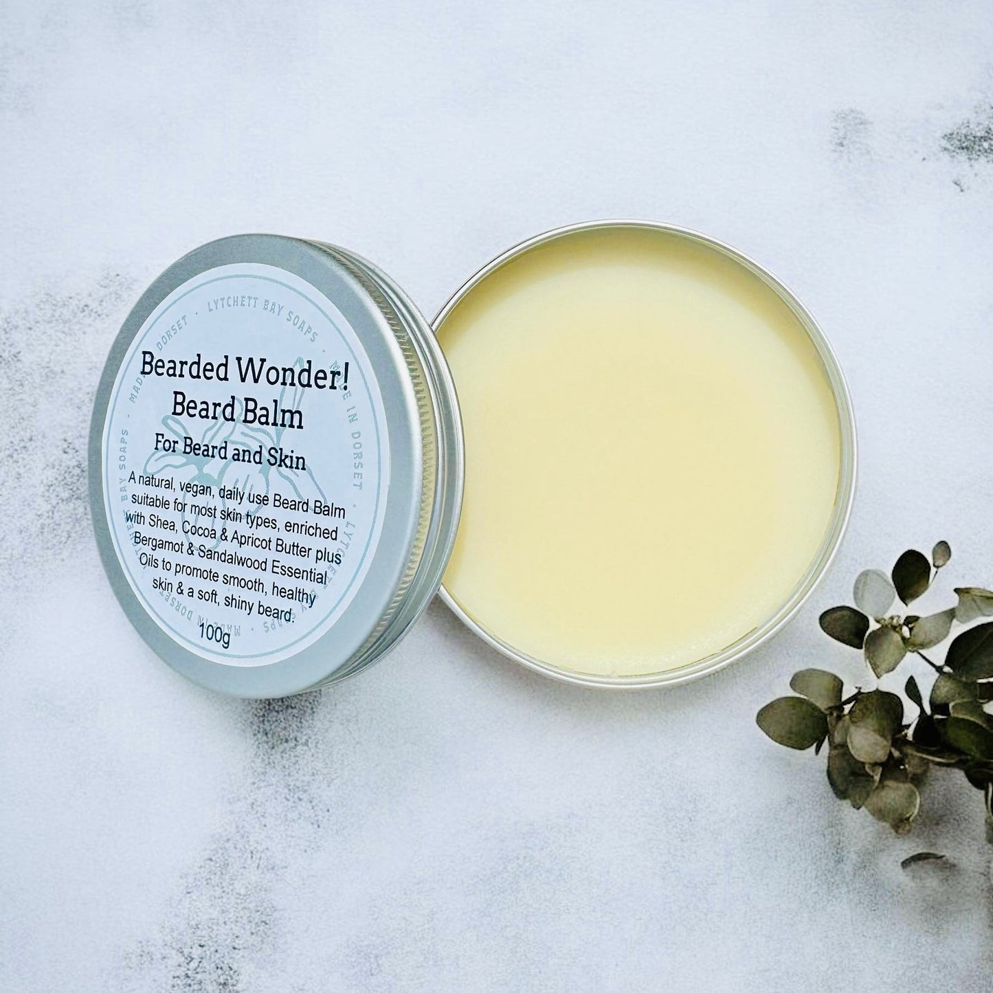 Bearded Wonder beard balm in a tin on a textured surface with eucalyptus leaves.
