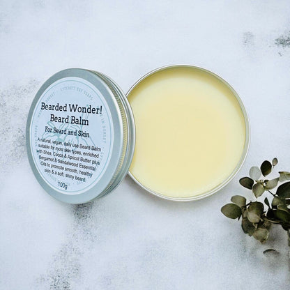 Bearded Wonder beard balm in a tin on a textured surface with eucalyptus leaves.