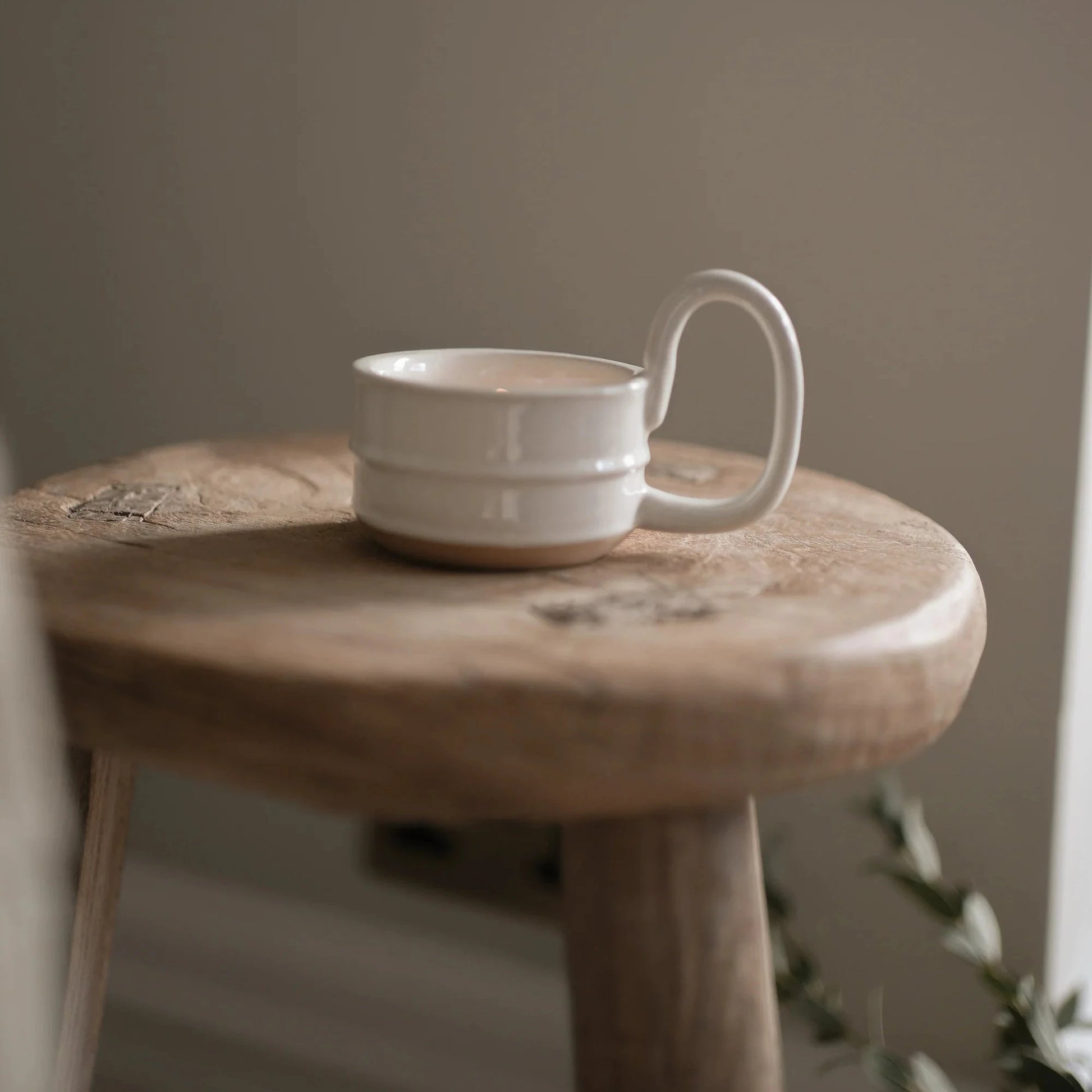 Indian artisanal hand glazed ceramic candle cup on a wooden stool against a plain wall.