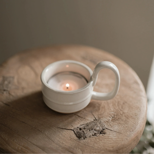 Milk white glazed ceramic candle holder with a small candle inside on a wooden surface.