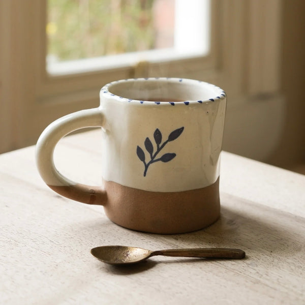 Hand painted natural stoneware ceramic mug with a botanic leaf design on a wooden surface next to an antique brass spoon. Rust Red Hand Painted Botanic Ceramic Mug | The Perfect Gift for Coffee Lovers.