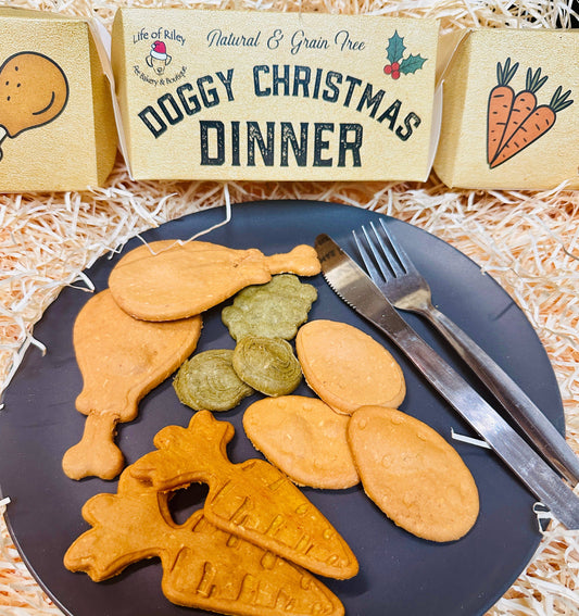 Doggy Christmas dinner cookies on a plate with a fork and knife, against a straw background with Christmas cracker in back of picture.