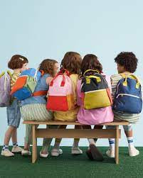 Children with colorful backpacks sitting on a bench against a light blue background