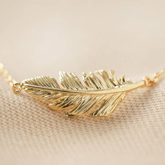 Gold feather-shaped necklace on a beige fabric background