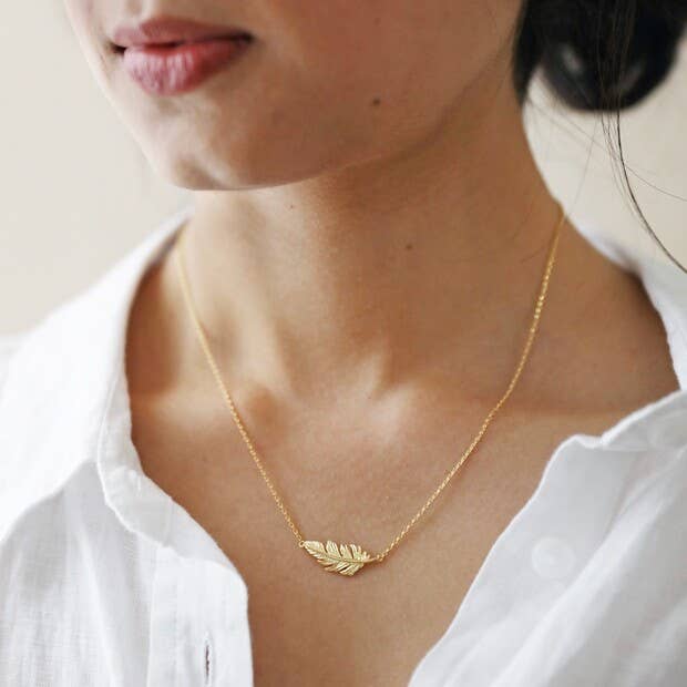 gold feather necklace worn by a girl wearing a crisply starched white collar shirt. The necklace lies perfectly across the collarbone.