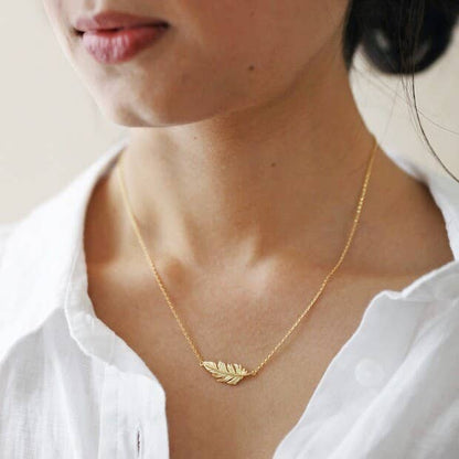 gold feather necklace worn by a girl wearing a crisply starched white collar shirt. The necklace lies perfectly across the collarbone.