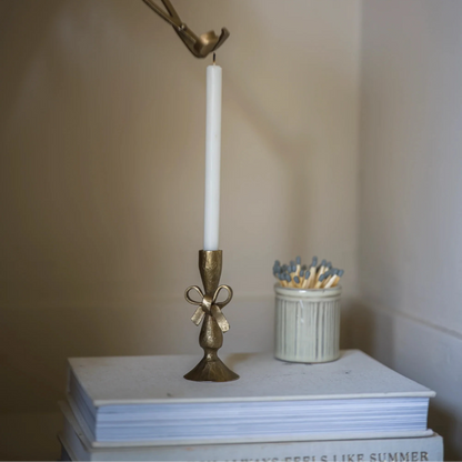 Bronze candle holder with a white candle on a stack of books against a plain background
