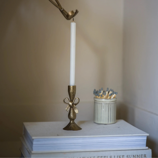 Bronze candle holder with a white candle on a stack of books against a plain background