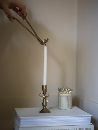 Bronze candle holder with a white candle on a stack of books against a plain background