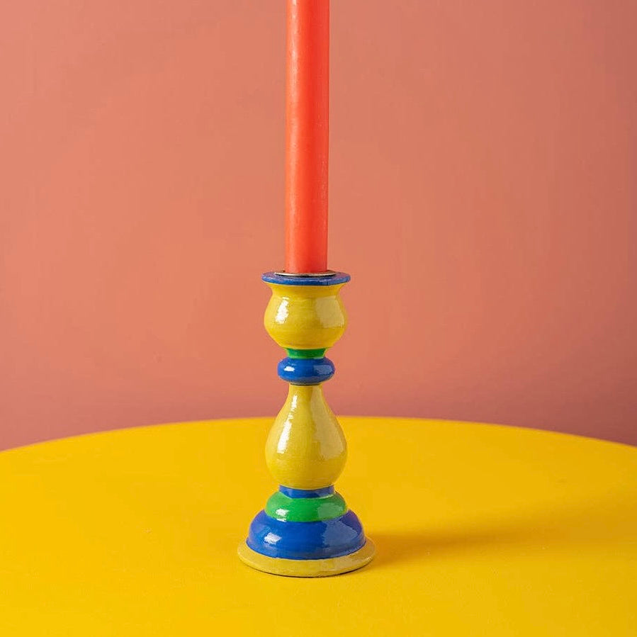 Ian Snow iconic shaped candle holder in olive green with dark green and cobalt contrasting rings. Featured holding a bright orange candle on a contrasting yellow surface and warm pink background. Part of SW Coast's Merry & Bright Christmas Collection.