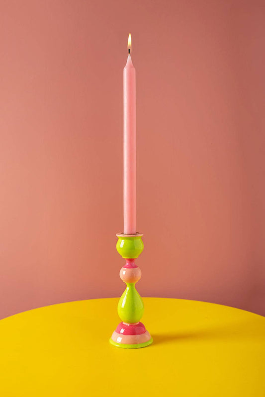 Colorful candle holder with a pink candle on a yellow surface and pink background