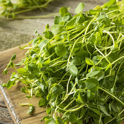 freshly cut pea shoots heaped loosely on a rustic farmers style chopping board.