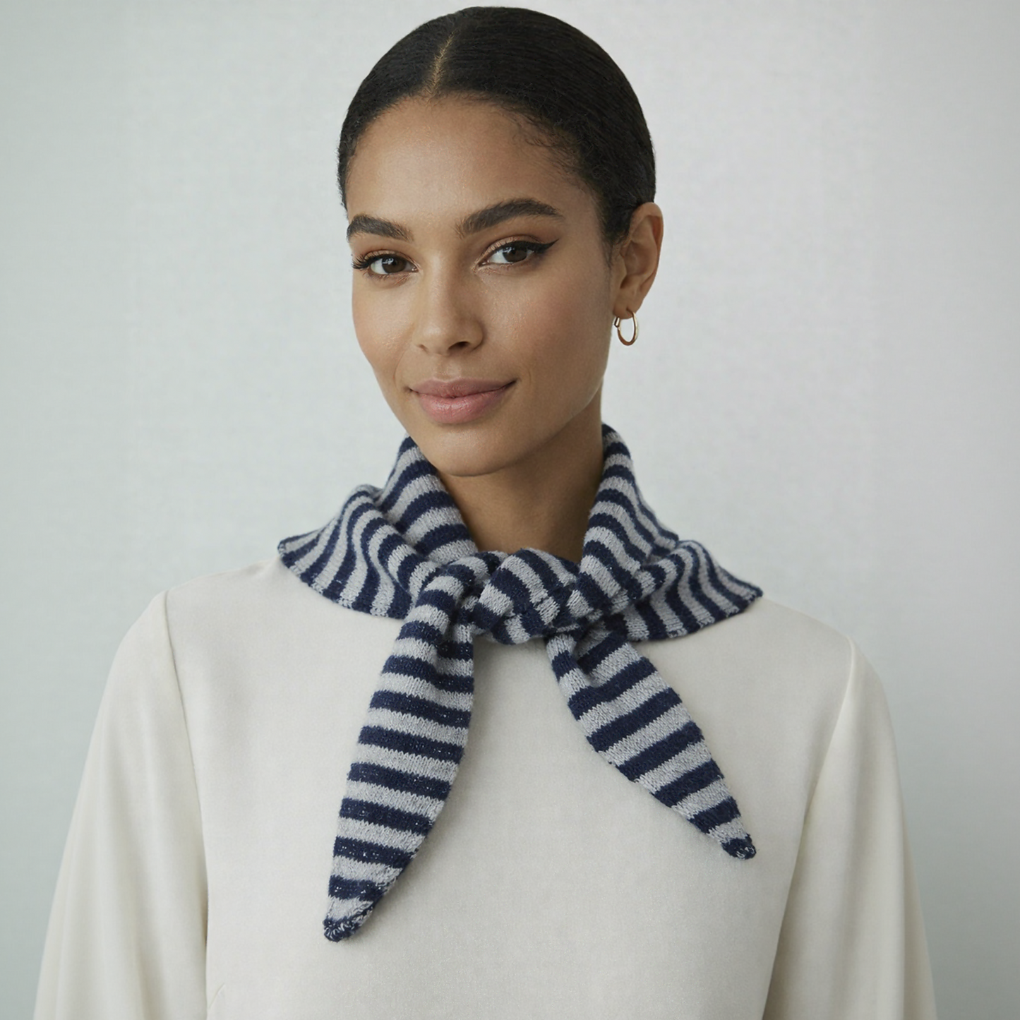 Model wearing a navy and white striped wool blend triangle neck scarf over a beige coat