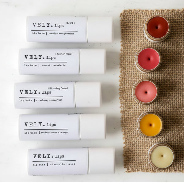 VELY lips tinted colourful lip balms in paper tube on a white surface with the tubes stood open on a piece of hessian, their colours displayed.