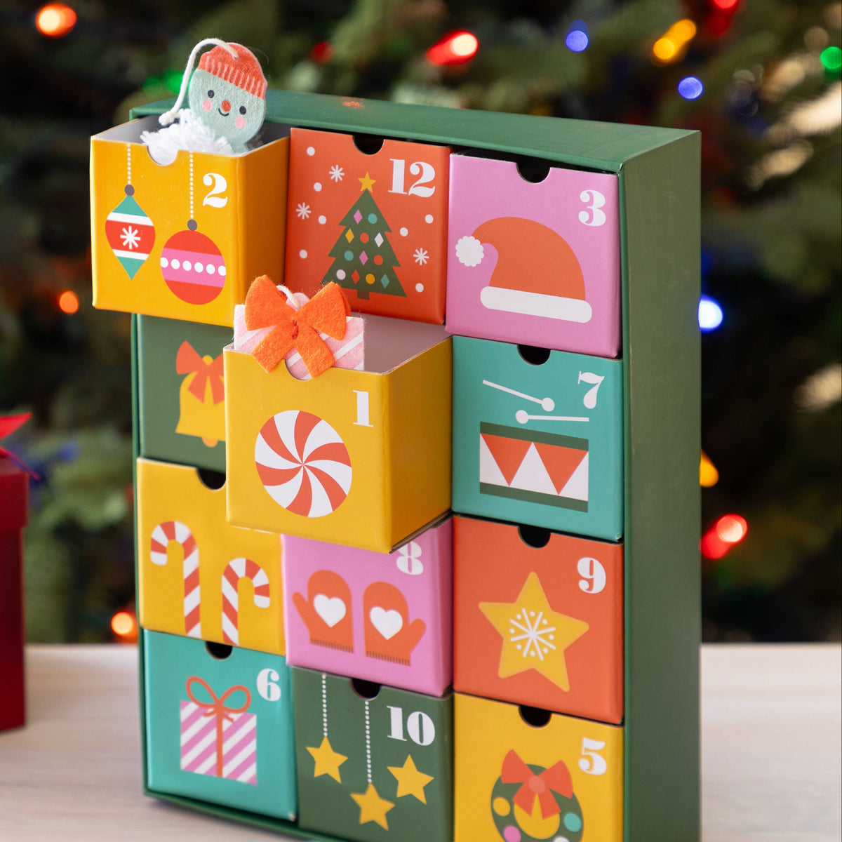 Colorful advent calendar with numbered drawers in front of a Christmas tree.